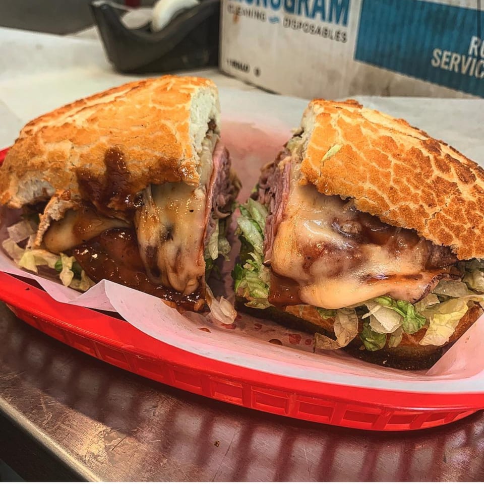 A Fast Eddie's Sandwich Shop sandwich, cut in half, with melted cheese, meat, and lettuce.