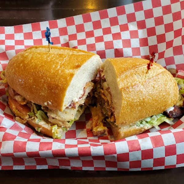 A Fast Eddie's Sandwich Shop sandwich, cut in half, filled with meat and lettuce, in a red and white checkered paper.