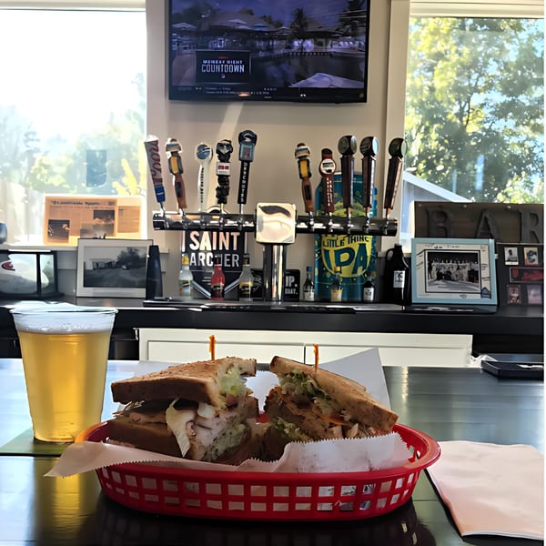 A Fast Eddie's sandwich in a red basket with a beer, bar taps, and a TV in the background.