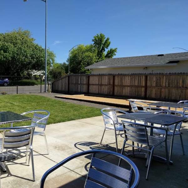 Outdoor patio with metal tables and chairs, a grassy area, and a bocce ball court.