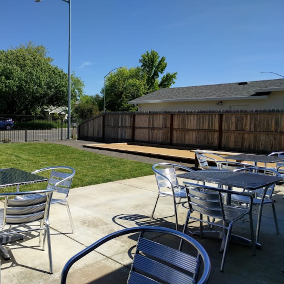 Outdoor patio with metal tables and chairs, a grassy area, and a bocce ball court.