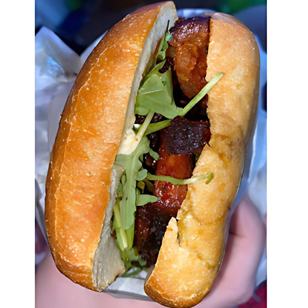 Close-up of a Fast Eddie's sandwich with dark meat, green arugula, and a golden-brown bun.