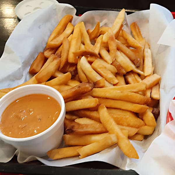 A basket of golden french fries with a side of orange dipping sauce from Fast Eddie's Sandwich Shop.